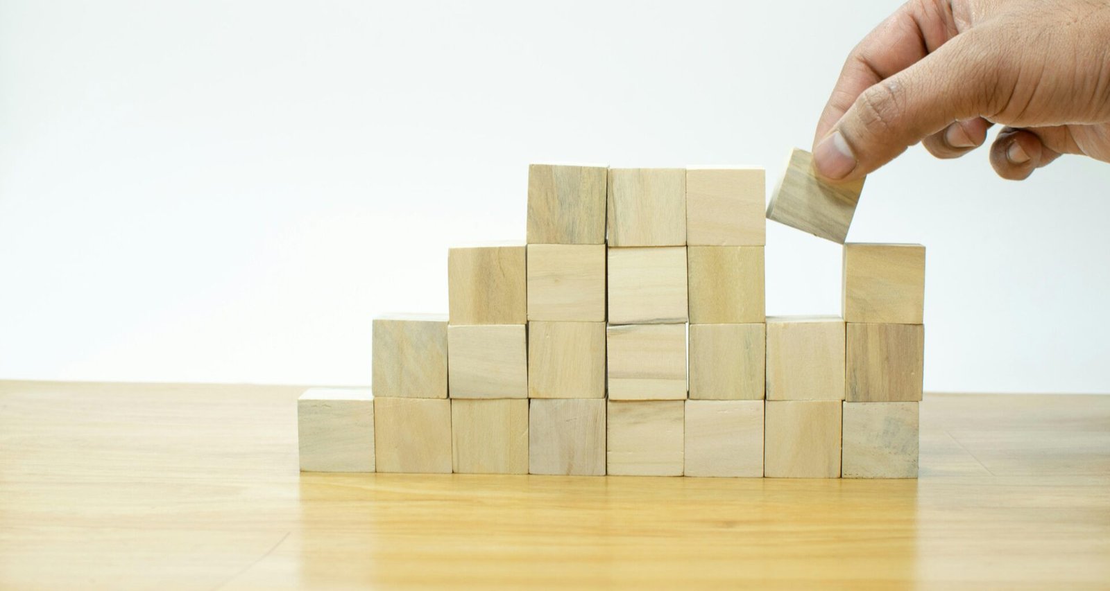 Eine Person platziert sorgfältig einen Holzblock auf einen Stapel aus mehreren Holzblöcken als Metapher für Unternehmensaufbau.