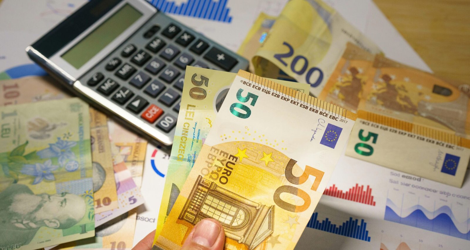 Eine Person hält mehrere Geldscheine in der Hand, neben einem Taschenrechner auf einem Tisch, Fokus auf Finanzverwaltung.