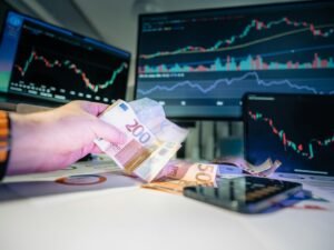 Eine Person hält Geldscheine vor einem Computerbildschirm, im Hintergrund ist eine Website zu sehen.