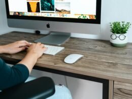 Eine Person sitzt an einem Schreibtisch mit Computer und arbeitet fokussiert in einem modernen Büro.