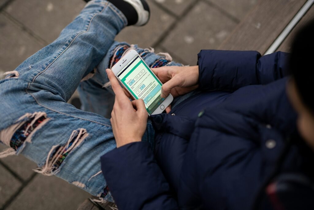 Person sitzt auf einer Bank und benutzt das Handy, Darstellung moderner mobiler Kommunikation im öffentlichen Raum