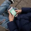Person sitzt auf einer Bank und benutzt das Handy, Darstellung moderner mobiler Kommunikation im öffentlichen Raum