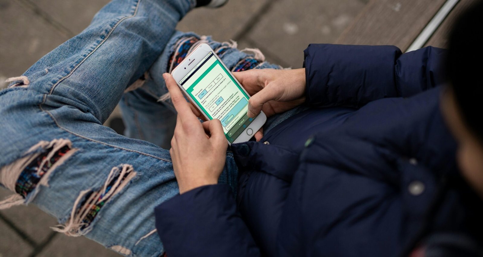 Person sitzt auf einer Bank und benutzt das Handy, Darstellung moderner mobiler Kommunikation im öffentlichen Raum