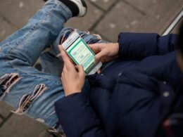 Person sitzt auf einer Bank und benutzt das Handy, Darstellung moderner mobiler Kommunikation im öffentlichen Raum