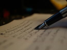 Eine Person schreibt mit einem Stift Notizen auf ein Blatt Papier am Schreibtisch, Fokus auf Hand und Papier