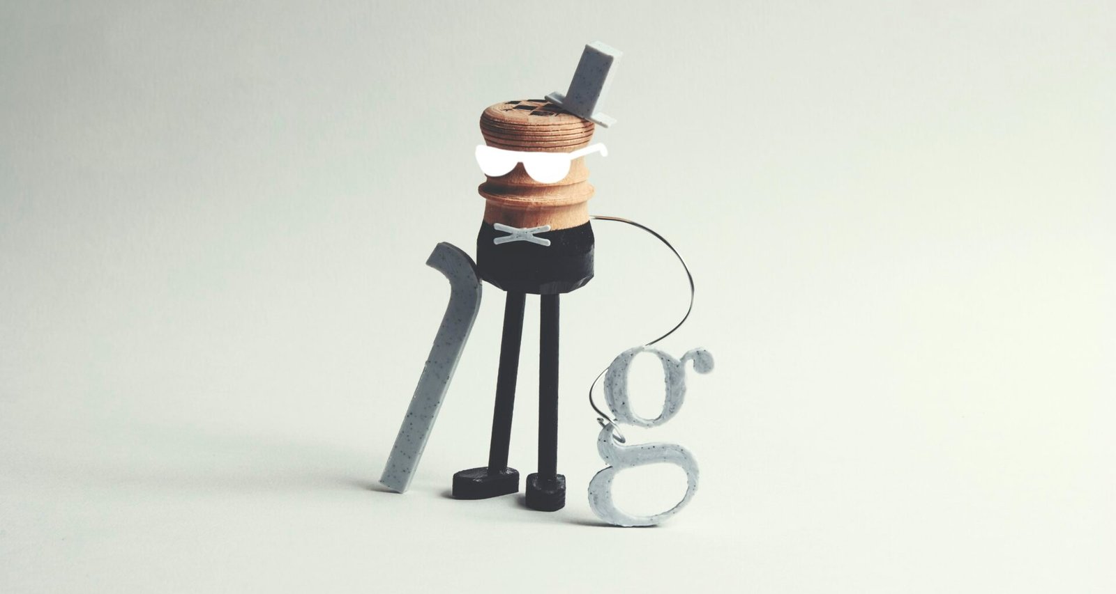 Eine ausgefallene Figur mit Stock und dem Buchstaben g als Accessoire, fotografiert vor neutralem Hintergrund