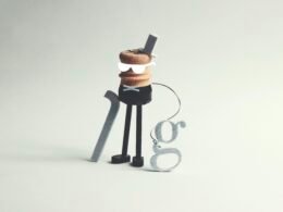 Eine ausgefallene Figur mit Stock und dem Buchstaben g als Accessoire, fotografiert vor neutralem Hintergrund