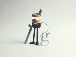 Eine ausgefallene Figur mit Stock und dem Buchstaben g als Accessoire, fotografiert vor neutralem Hintergrund