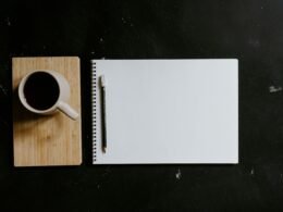 Eine Tasse Kaffee neben einem geöffneten Notizbuch und einem Stift auf einem modernen Schreibtisch