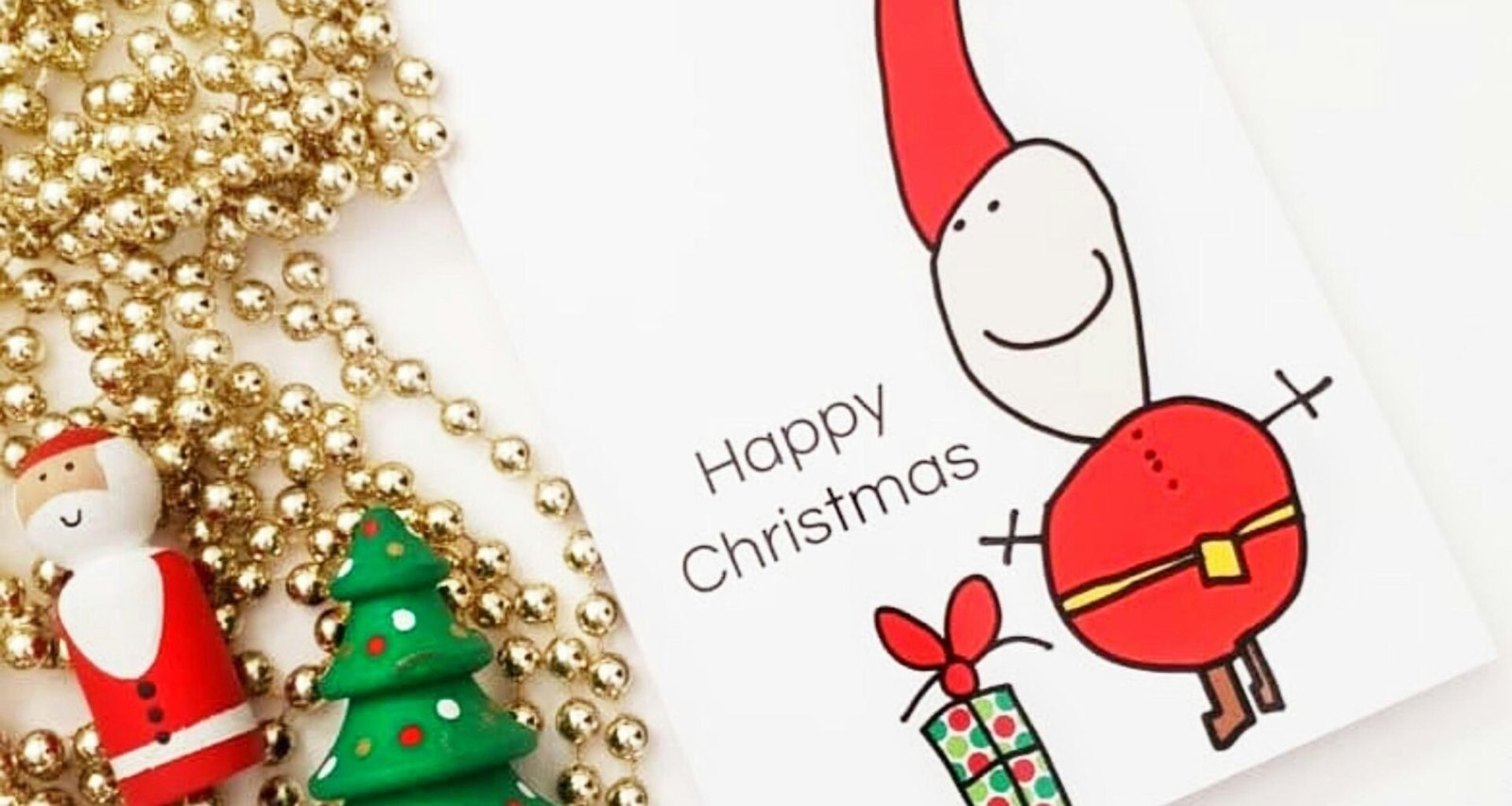 Eine Weihnachtskarte liegt auf einem Tisch neben einem geschmückten Weihnachtsbaum mit Lichtern und Kugeln.