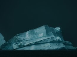 Großer weißer Eisberg treibt auf dunklem Wasser, aufgenommen von Matthew Stephenson, klare Struktur und kalte Farben