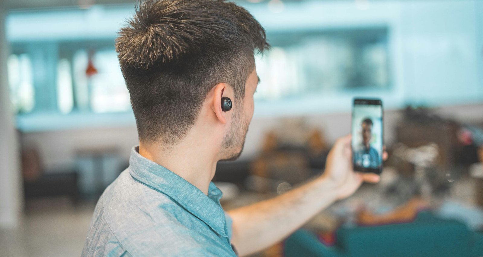 Mann mit grauem, kragenbesetztem Oberteil nimmt mit Smartphone ein Selfie in moderner Umgebung auf