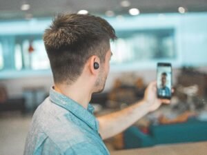 Mann mit grauem, kragenbesetztem Oberteil nimmt mit Smartphone ein Selfie in moderner Umgebung auf