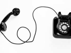 Schwarzes Retro-Wählscheibentelefon steht vor schlicht weißem Hintergrund, symbolisiert klassische Kommunikationstechnik.