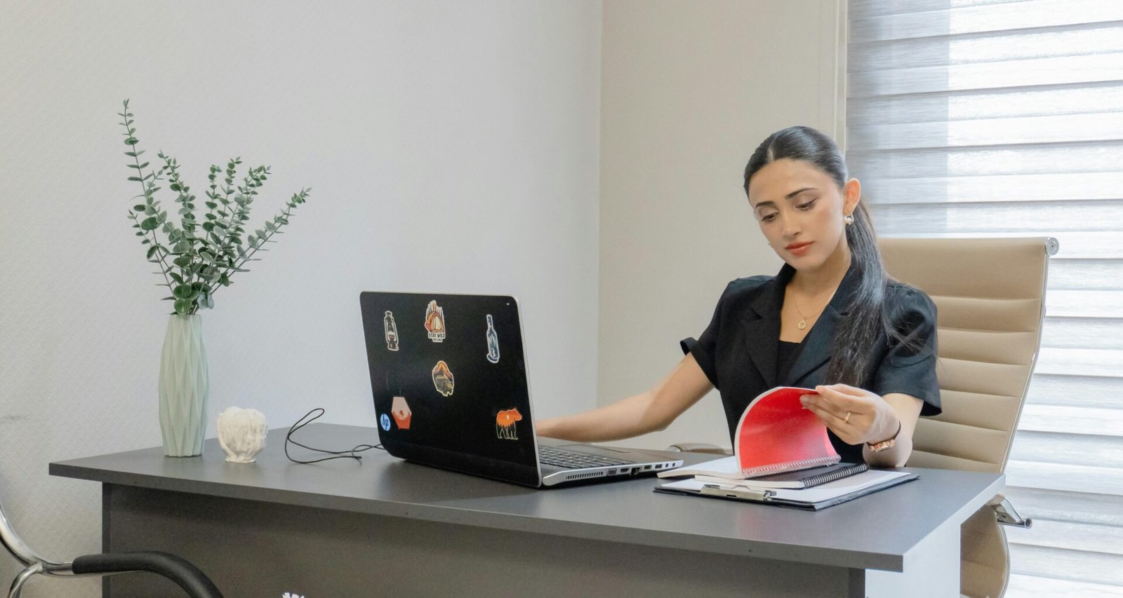Frau sitzt am Schreibtisch, arbeitet am Laptop und liest Unterlagen – modernes Arbeitsumfeld in einem Büro.