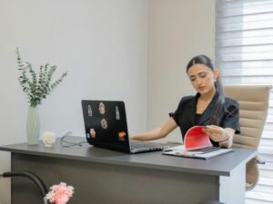 Frau sitzt am Schreibtisch, arbeitet am Laptop und liest Unterlagen – modernes Arbeitsumfeld in einem Büro.