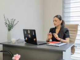 Frau sitzt an einem Schreibtisch und arbeitet an einem Laptop in einem gut beleuchteten Raum