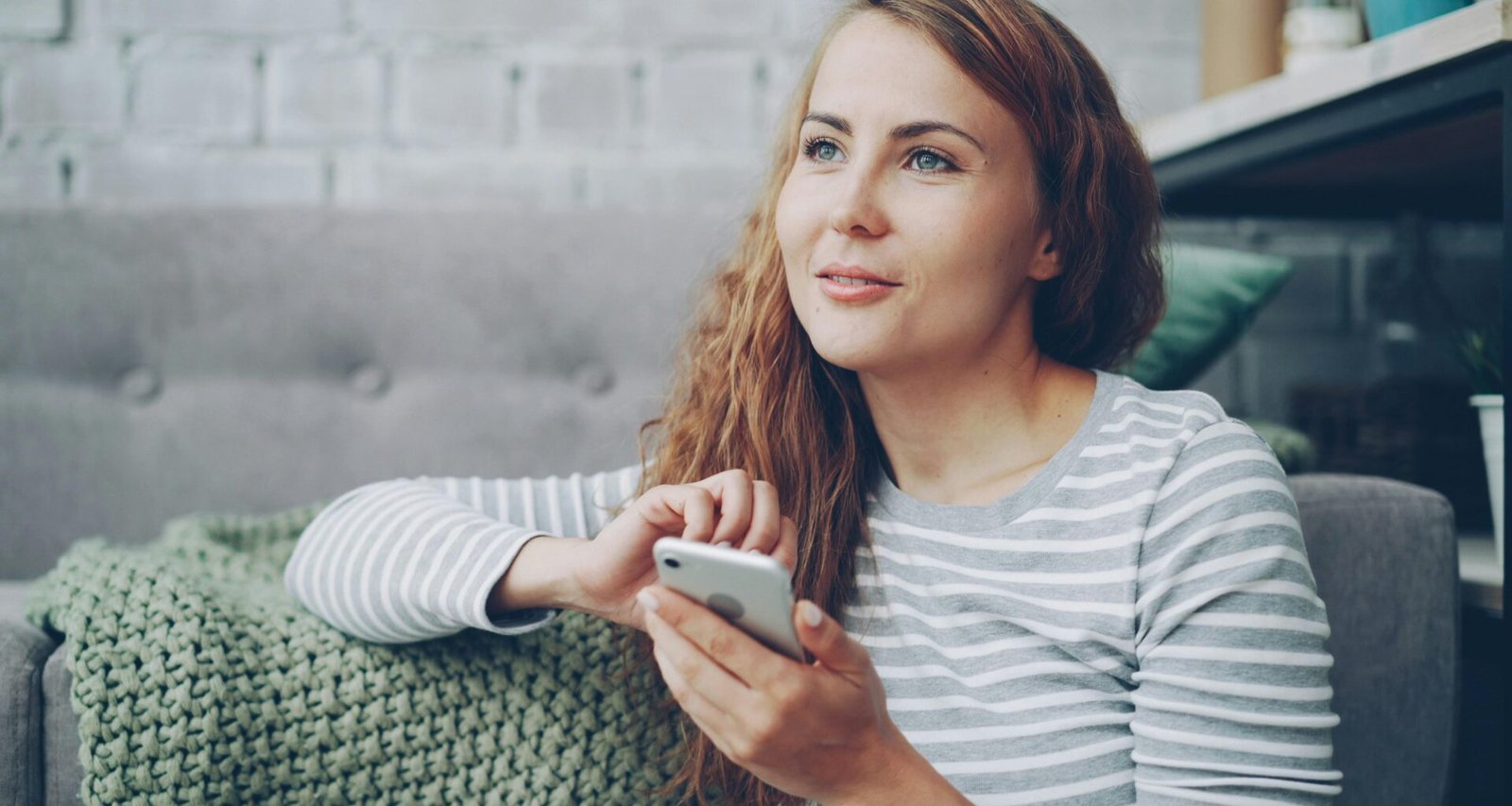 Frau sitzt auf einem Sofa und hält ein Smartphone in der Hand, während sie auf den Bildschirm schaut