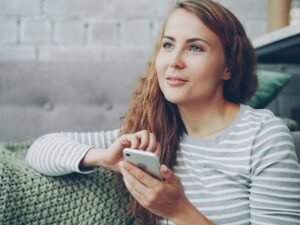Frau sitzt auf einem Sofa und hält ein Smartphone in der Hand, während sie auf den Bildschirm schaut