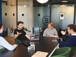 Zwei Frauen sitzen nebeneinander an einem Tisch und arbeiten gemeinsam mit Laptops in einem modernen Büro