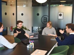 Zwei Frauen sitzen nebeneinander an einem Tisch und arbeiten gemeinsam mit Laptops in einem modernen Büro