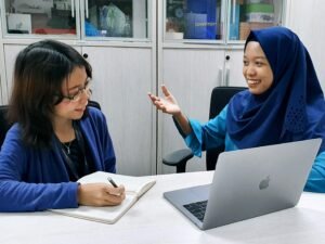 Frau in blauem Bademantel sitzt am Tisch und nutzt ein MacBook, arbeitet fokussiert von zu Hause aus am Laptop