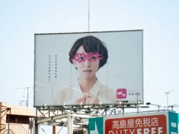 Frau in weißem und pinkem Blumenkleid steht vor einem Whiteboard und erklärt Inhalte in einem modernen Büro.