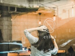 Frau im weiß-schwarzen Langarmshirt sitzt auf einem Stuhl vor einem Schreibtisch im Büro, Blick auf Arbeitsumgebung