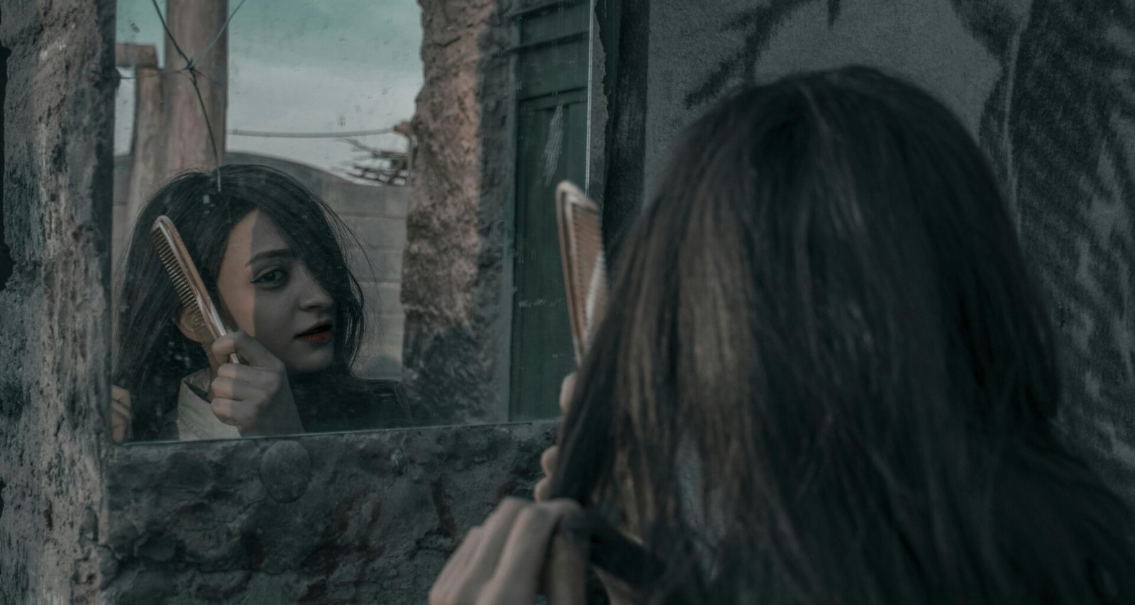 Junge Frau kämmt ihre glatten, langen Haare vor einem neutralen Hintergrund – Fokus auf Haarpflege