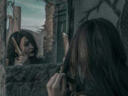 Junge Frau kämmt ihre glatten, langen Haare vor einem neutralen Hintergrund – Fokus auf Haarpflege