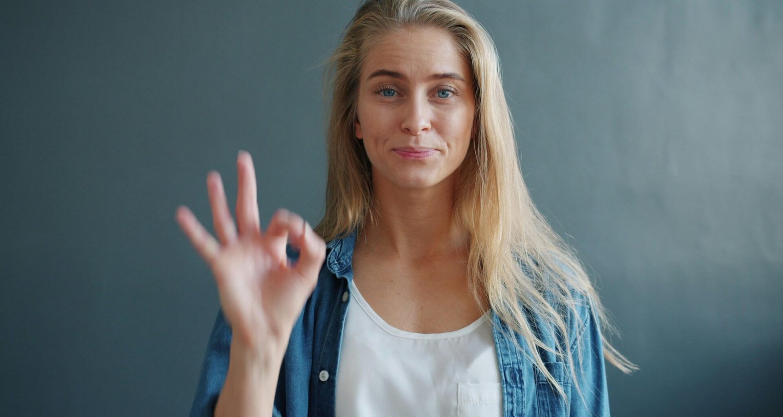 Frau zeigt das Ok-Zeichen mit der Hand vor neutralem Hintergrund, passend zu Kommunikations- oder Technikthemen