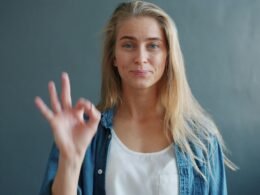 Frau zeigt das Ok-Zeichen mit der Hand vor neutralem Hintergrund, passend zu Kommunikations- oder Technikthemen