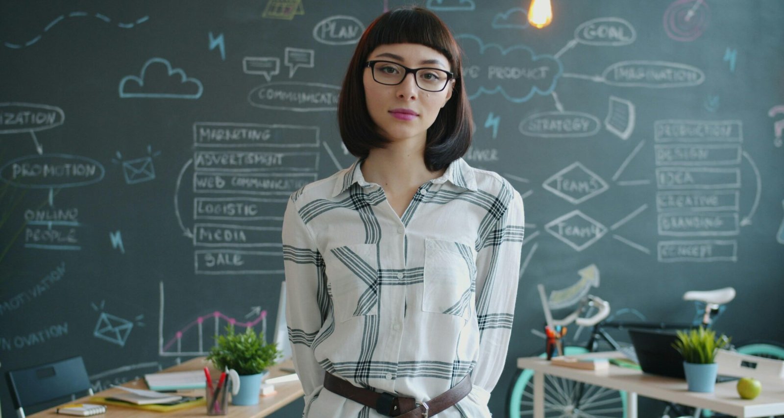 Frau steht vor einer Kreidetafel mit grafischen Diagrammen und erklärt Inhalte, Fokus auf Wissenstransfer und Präsentation