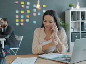 Frau sitzt am Schreibtisch, telefoniert und nutzt einen Laptop in einem modernen Arbeitsumfeld