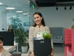 Frau verlässt das Büro und trägt eine Kiste mit persönlichen Sachen als Zeichen für einen beruflichen Umbruch