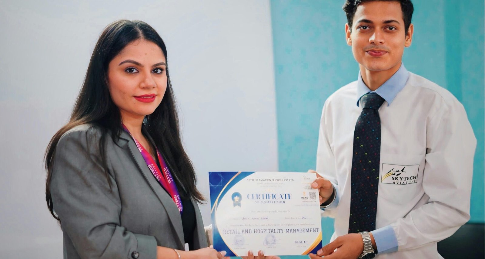 Frau übergibt im Büro einem Mann ein Zertifikat, beide stehen an einem Schreibtisch und wirken professionell