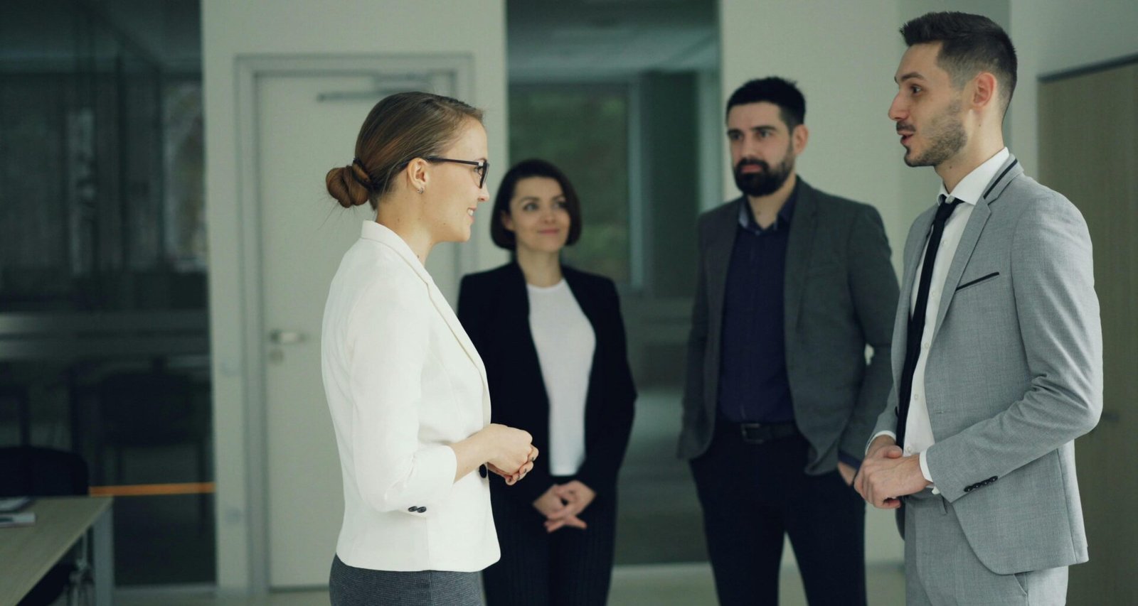 Geschäftsleute sprechen miteinander in einem offenen, modernen Büroflur mit Glaswänden und hellen Räumen.