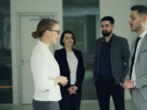 Geschäftsleute sprechen miteinander in einem offenen, modernen Büroflur mit Glaswänden und hellen Räumen.