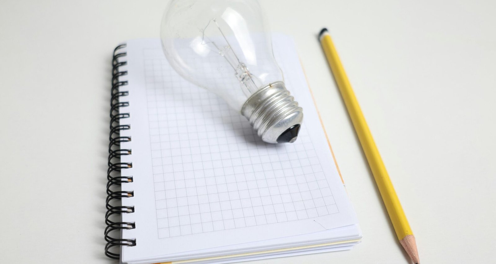 Eine Glühbirne und ein Bleistift liegen nebeneinander auf einem Notizblock, fotografiert für einen Technik-Artikel.