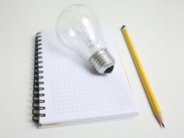 Eine Glühbirne und ein Bleistift liegen nebeneinander auf einem Notizblock, fotografiert für einen Technik-Artikel.