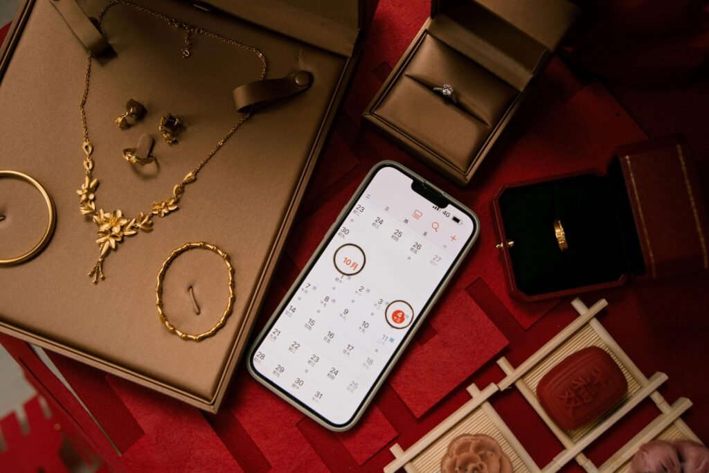 Goldene Schmuckstücke, darunter Ringe, werden zusammen mit einem Smartphone auf einer Oberfläche arrangiert präsentiert.