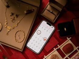 Goldene Schmuckstücke, darunter Ringe, werden zusammen mit einem Smartphone auf einer Oberfläche arrangiert präsentiert.