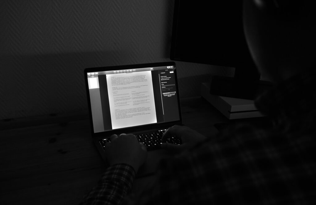 Grayscale-Foto einer Person, die an einem MacBook Pro arbeitet, konzentriert am Laptop an einem modernen Arbeitsplatz