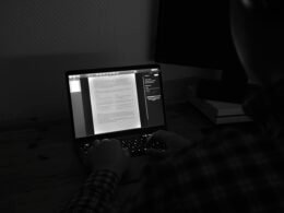 Grayscale-Foto einer Person, die an einem MacBook Pro arbeitet, konzentriert am Laptop an einem modernen Arbeitsplatz