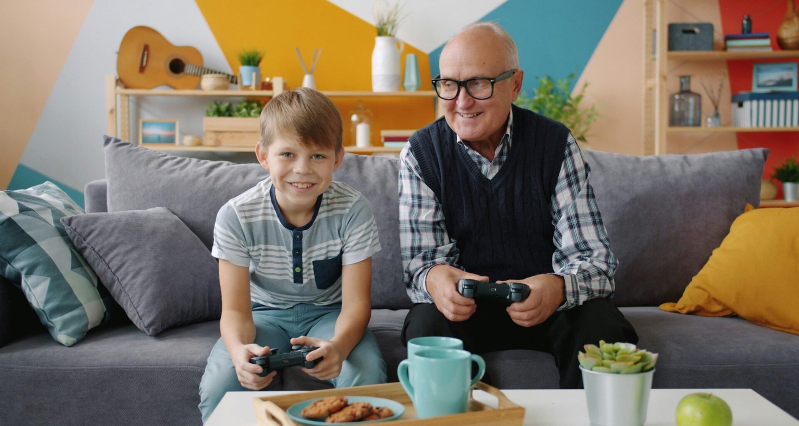 Ein älterer Mann und ein Junge sitzen auf einem Sofa und spielen gemeinsam Videospiele mit Controllern.