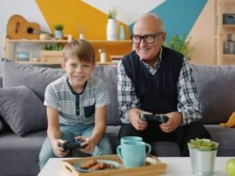 Ein älterer Mann und ein Junge sitzen auf einem Sofa und spielen gemeinsam Videospiele mit Controllern.