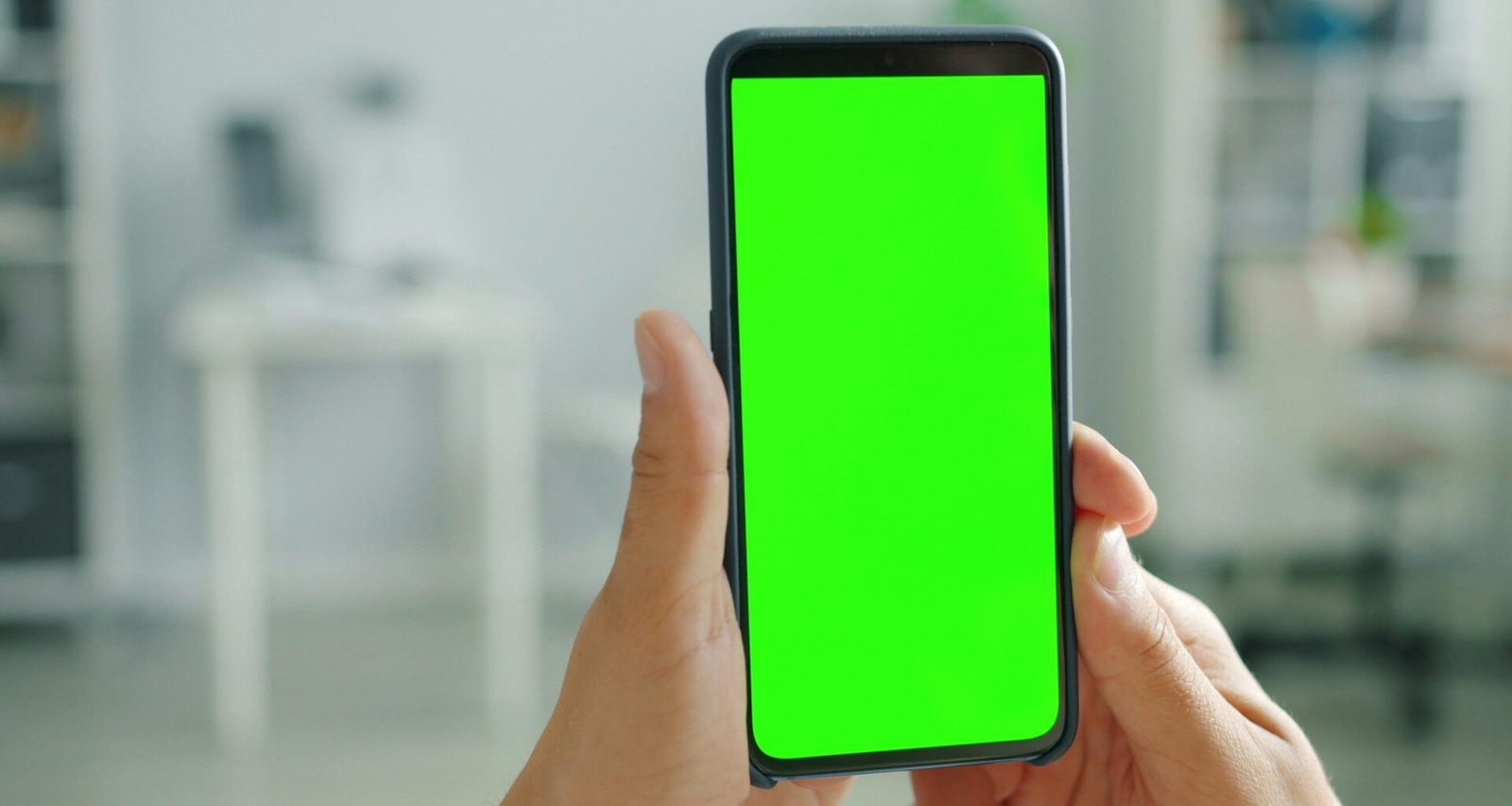 Zwei Hände halten ein Smartphone mit grünem Bildschirm vor neutralem Hintergrund – Fokus auf mobile Endgeräte.