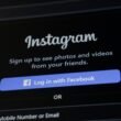 Smartphone zeigt Instagram-Anmeldebildschirm mit Facebook-Login-Option auf weißem Hintergrund.