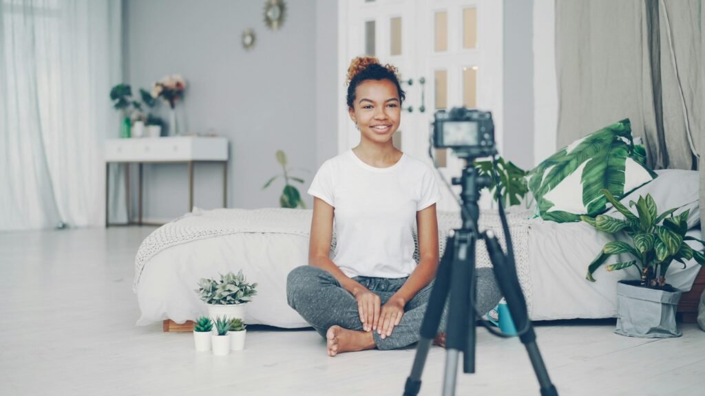 Junge Frau sitzt auf dem Boden und filmt mit einer digitalen Kamera für kreative Projekte in Innenraum