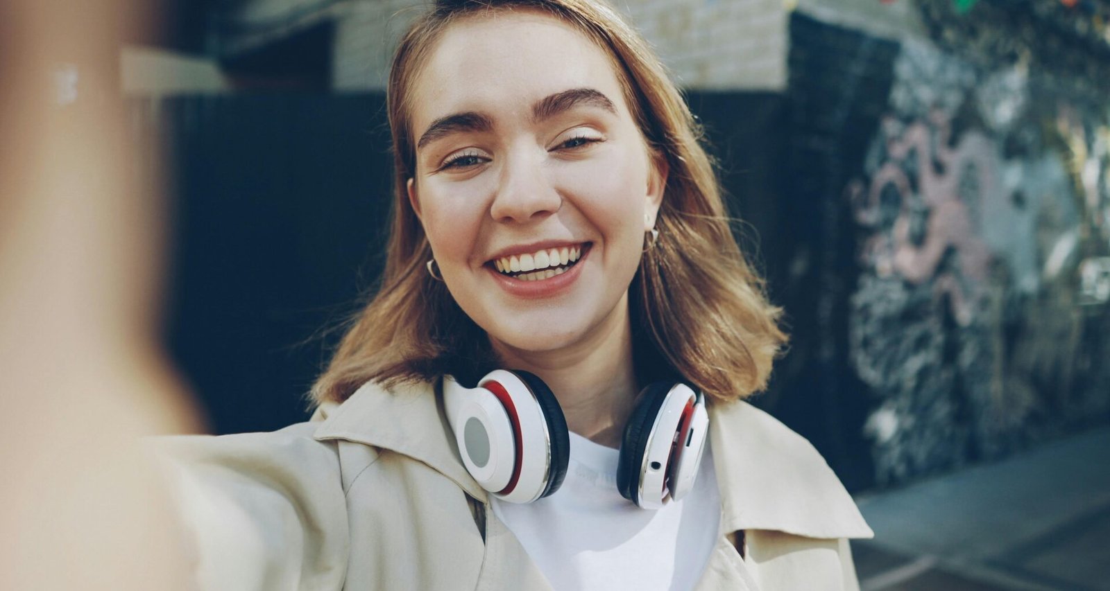 Junge Frau lächelt und fotografiert sich mit dem Smartphone beim Selfie im Freien, Fokus auf natürliche Umgebung.